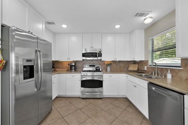 kitchen featuring stainless steel appliances, sink, white cabinetry, light tile patterned floors, and tasteful backsplash