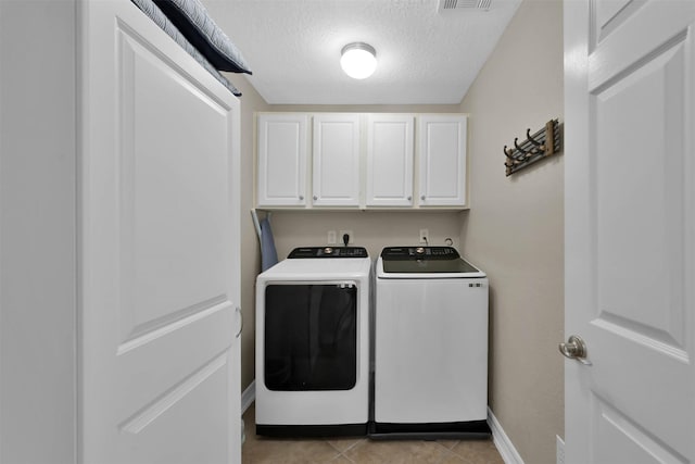 washroom featuring light tile patterned floors, washing machine and dryer, cabinets, and a textured ceiling