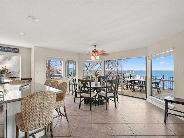 tiled dining area featuring a textured ceiling, ceiling fan, and a water view