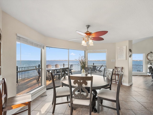 dining space featuring ceiling fan, light tile patterned floors, and a water view