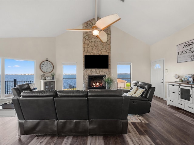 living room featuring dark hardwood / wood-style floors, high vaulted ceiling, a fireplace, ceiling fan, and a water view