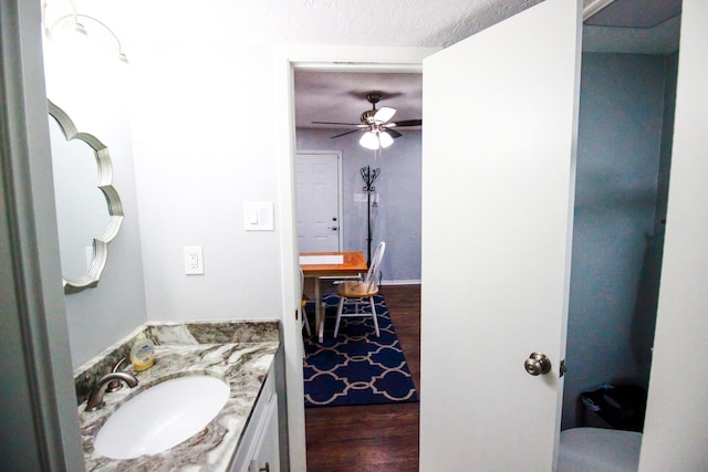 bathroom featuring vanity with extensive cabinet space, a textured ceiling, wood-type flooring, and ceiling fan