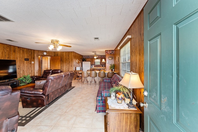 living room with wooden walls, ceiling fan, and light tile patterned floors