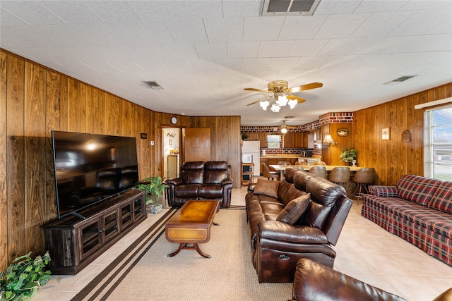 tiled living room featuring ceiling fan and wooden walls