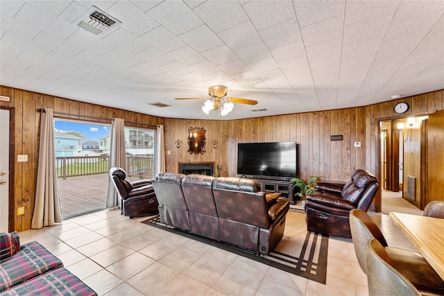 living room featuring ceiling fan, light tile patterned floors, a fireplace, and wooden walls