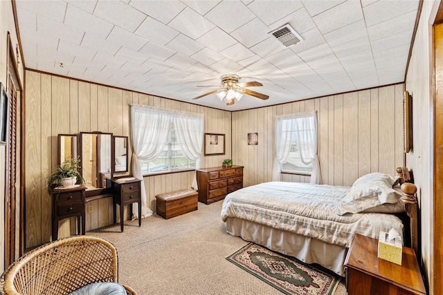 bedroom with ceiling fan, wooden walls, and light colored carpet