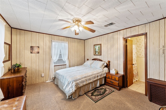 carpeted bedroom with ensuite bath, ceiling fan, and wood walls