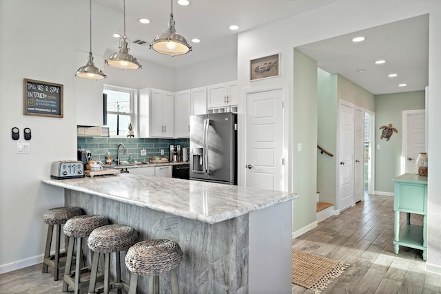 kitchen with light stone countertops, backsplash, light hardwood / wood-style flooring, stainless steel refrigerator with ice dispenser, and white cabinets