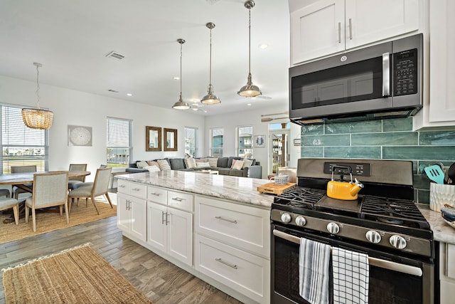 kitchen with light stone countertops, appliances with stainless steel finishes, backsplash, white cabinetry, and pendant lighting