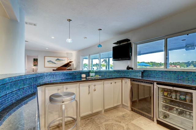 kitchen with wine cooler, hanging light fixtures, tasteful backsplash, and white cabinets