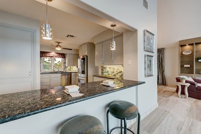 kitchen featuring appliances with stainless steel finishes, a kitchen bar, decorative backsplash, hanging light fixtures, and kitchen peninsula