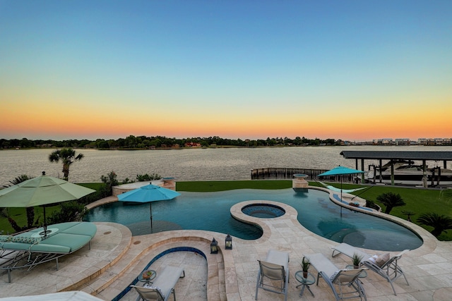 pool at dusk featuring a patio area, an in ground hot tub, and a water view