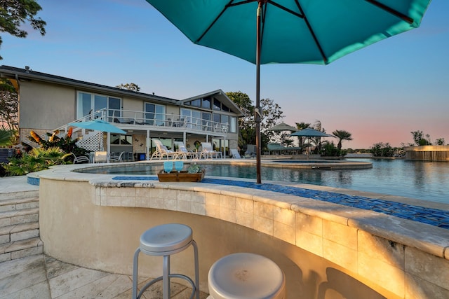 pool at dusk with a patio area and a hot tub