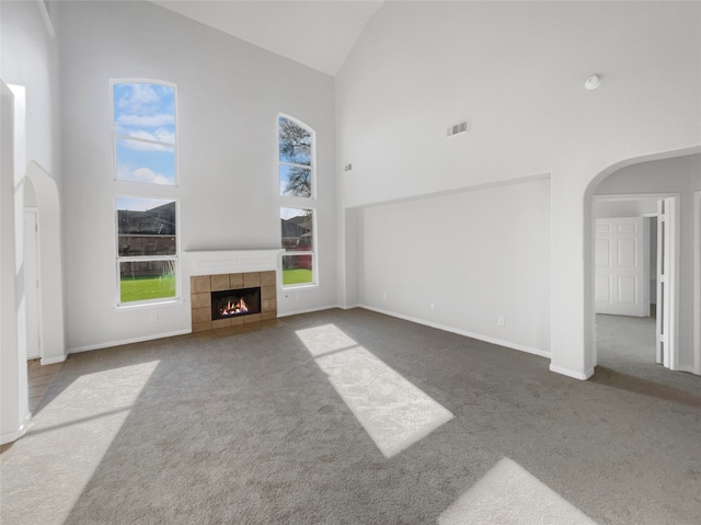 unfurnished living room with dark colored carpet, a tile fireplace, and high vaulted ceiling