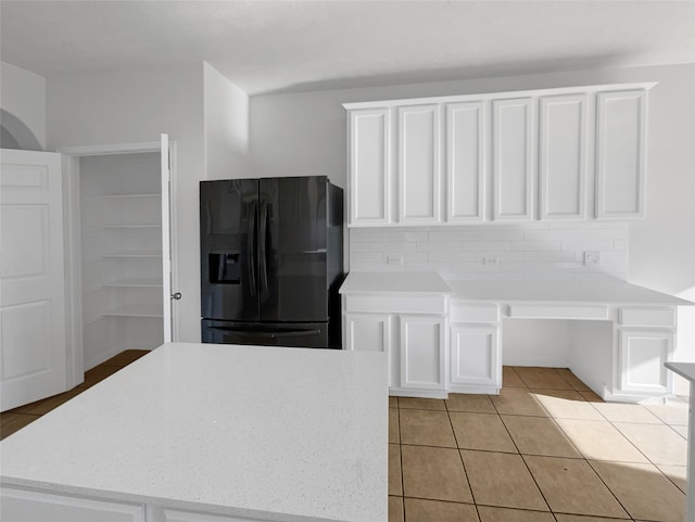 kitchen featuring tasteful backsplash, a kitchen island, light tile floors, black fridge with ice dispenser, and white cabinets