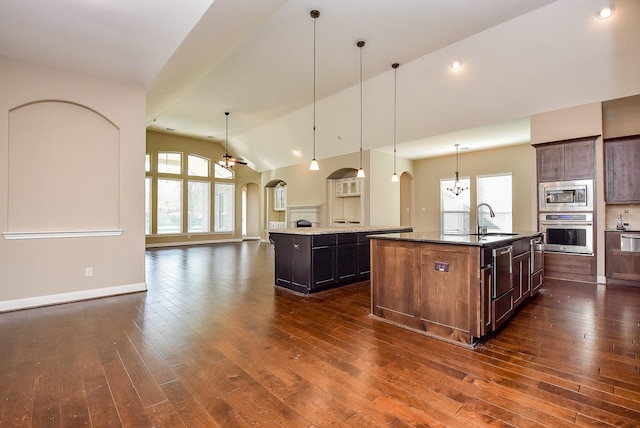 kitchen featuring ceiling fan, hanging light fixtures, an island with sink, vaulted ceiling, and appliances with stainless steel finishes