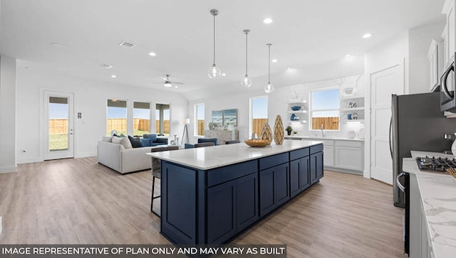 kitchen featuring light stone countertops, appliances with stainless steel finishes, ceiling fan, a center island, and white cabinetry