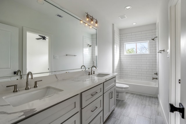 full bathroom with double sink, ceiling fan, tiled shower / bath, vanity with extensive cabinet space, and toilet