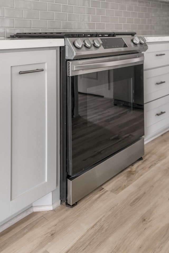 room details featuring tasteful backsplash, stainless steel electric stove, and light hardwood / wood-style floors