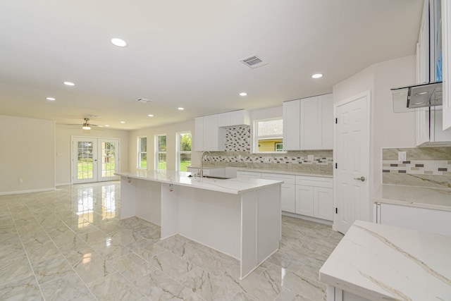 kitchen with decorative backsplash, a kitchen island with sink, ceiling fan, and white cabinetry