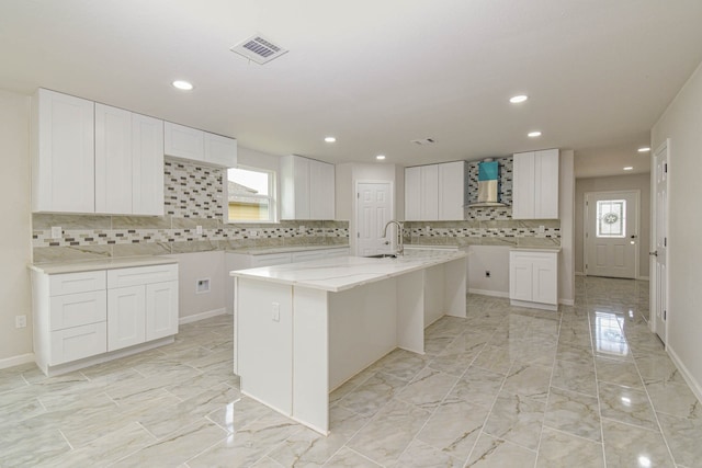 kitchen with white cabinets, backsplash, and a kitchen island with sink