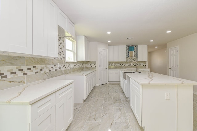 kitchen with wall chimney exhaust hood, a large island with sink, light stone counters, and white cabinets