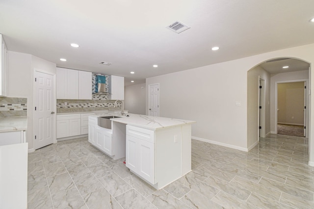 kitchen featuring a kitchen island with sink, sink, white cabinetry, wall chimney exhaust hood, and decorative backsplash