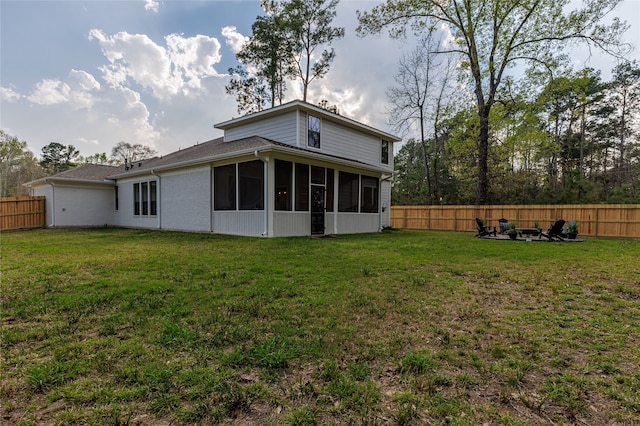 back of property featuring a sunroom, a yard, and an outdoor fire pit