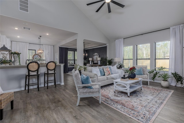 living room with a wealth of natural light, high vaulted ceiling, dark wood-type flooring, and ceiling fan with notable chandelier