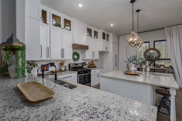 kitchen with light stone countertops, white cabinetry, stainless steel gas stove, sink, and pendant lighting