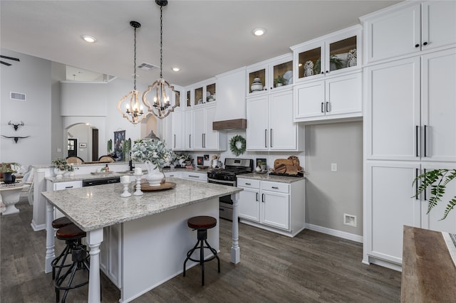 kitchen with a center island, stainless steel gas range oven, white cabinets, light stone countertops, and decorative light fixtures