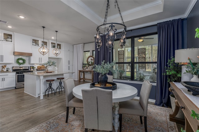 dining room with ceiling fan with notable chandelier, a raised ceiling, ornamental molding, and light hardwood / wood-style flooring