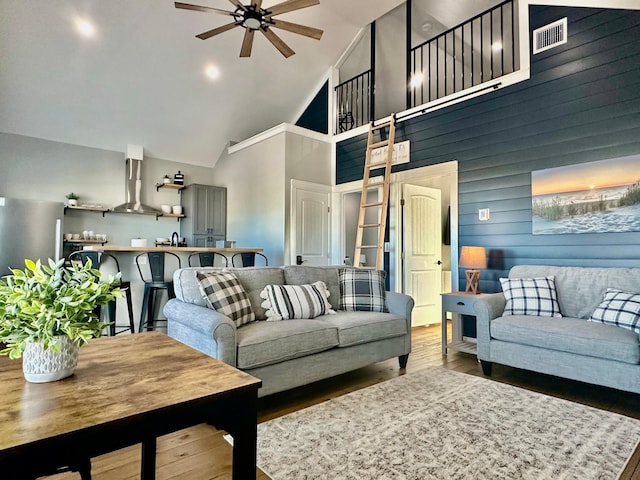 living room with high vaulted ceiling, hardwood / wood-style floors, ceiling fan, and wood walls