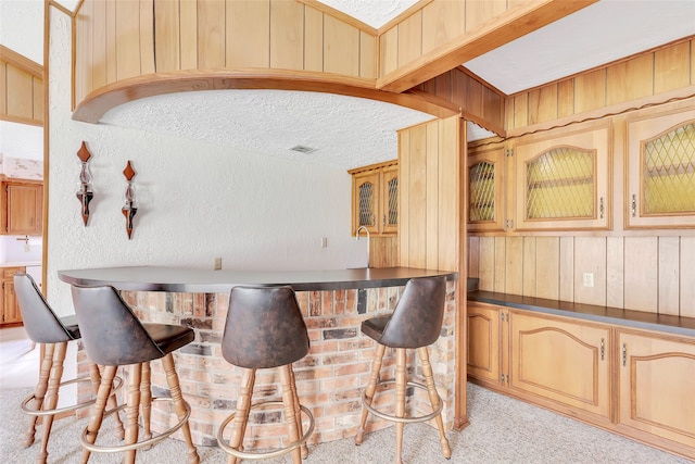 bar featuring light carpet, beam ceiling, a textured ceiling, and wood walls