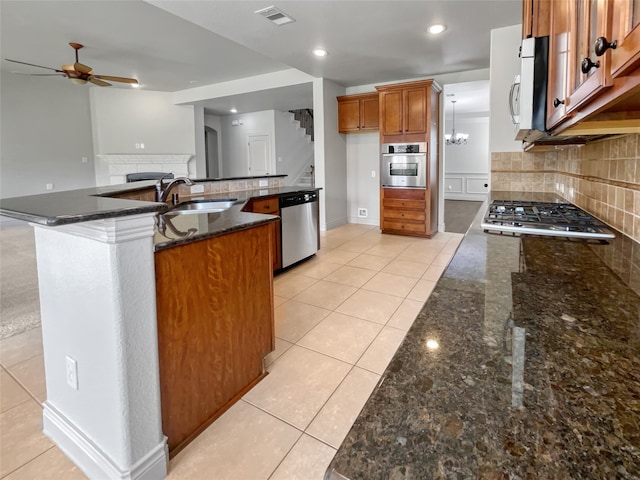 kitchen with sink, backsplash, stainless steel appliances, light tile flooring, and ceiling fan with notable chandelier