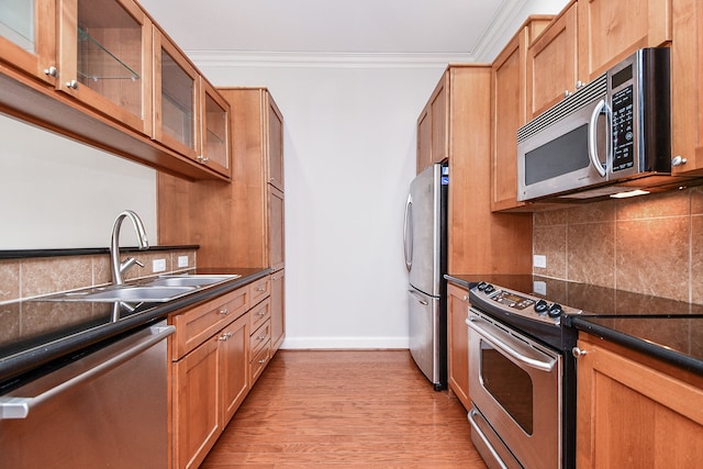 kitchen with tasteful backsplash, crown molding, stainless steel appliances, light wood-type flooring, and sink