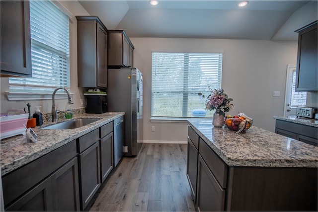 kitchen featuring light stone counters, sink, lofted ceiling, a kitchen island, and light hardwood / wood-style flooring