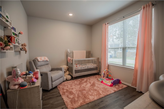 bedroom with multiple windows, a nursery area, and dark hardwood / wood-style flooring