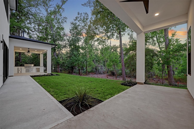 yard at dusk with area for grilling, ceiling fan, and a patio area