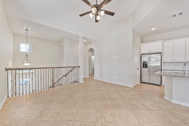 interior space with white cabinets, ceiling fan, light stone countertops, backsplash, and stainless steel refrigerator with ice dispenser