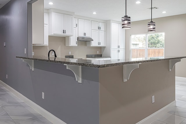 kitchen with white cabinets, a breakfast bar, hanging light fixtures, and dark stone counters