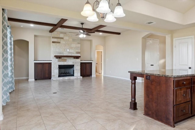 interior space with ceiling fan with notable chandelier, beam ceiling, a stone fireplace, and light tile patterned floors