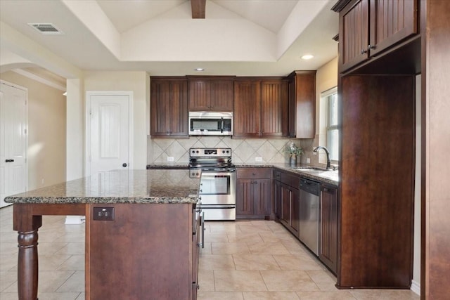 kitchen with appliances with stainless steel finishes, dark stone counters, vaulted ceiling, sink, and a kitchen island