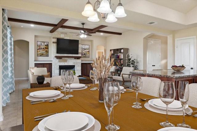 dining space featuring coffered ceiling, ceiling fan with notable chandelier, light tile patterned floors, beamed ceiling, and a stone fireplace