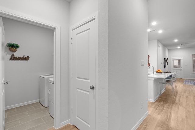 hallway with sink, washer and dryer, and light hardwood / wood-style floors