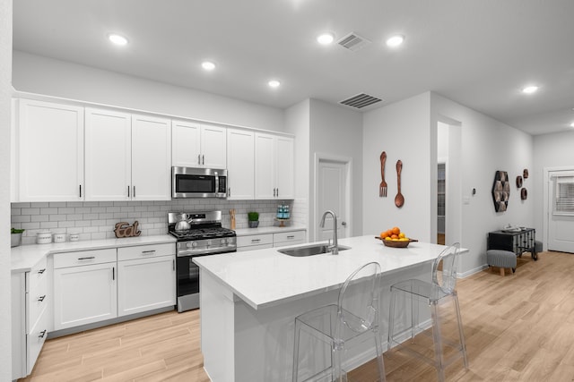 kitchen with appliances with stainless steel finishes, sink, white cabinets, light hardwood / wood-style floors, and an island with sink