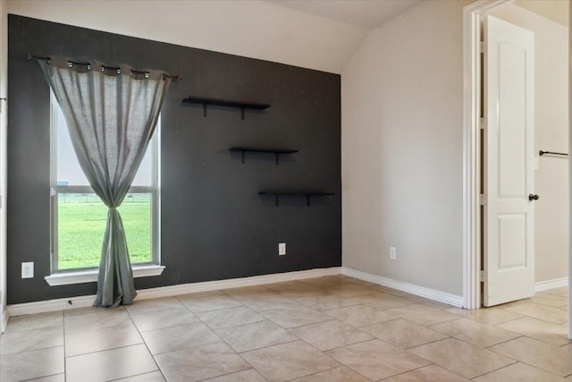 tiled empty room featuring vaulted ceiling