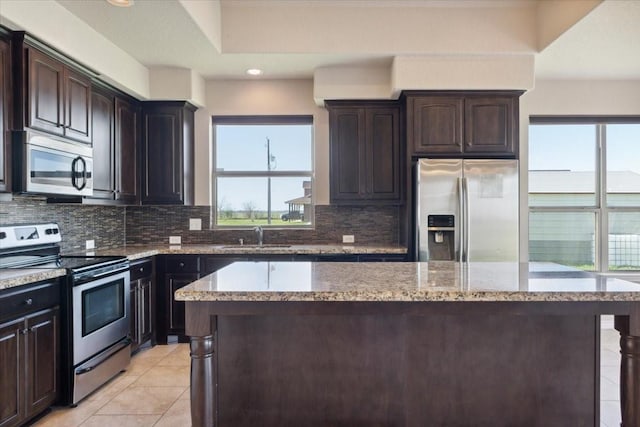 kitchen with light stone countertops, backsplash, dark brown cabinetry, stainless steel appliances, and sink