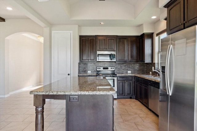 kitchen with appliances with stainless steel finishes, backsplash, light stone counters, sink, and a kitchen island