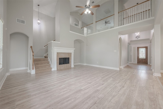 unfurnished living room featuring ceiling fan, a high ceiling, light wood-type flooring, and a tiled fireplace